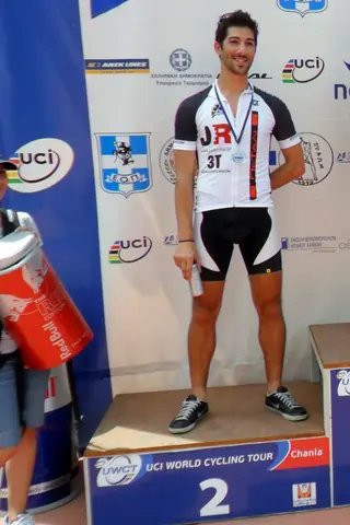 Kostis on the second-place step of the Men’s Elite podium at a UCI World Cycling Tour race in Chania, Crete, medal on, UCI banners behind