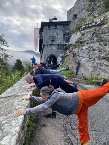 Kostis and fellow Shaolin students in a line along the wall of Burg Finstergrün, Austria, each kicking one leg high behind them, the castle gate tower above