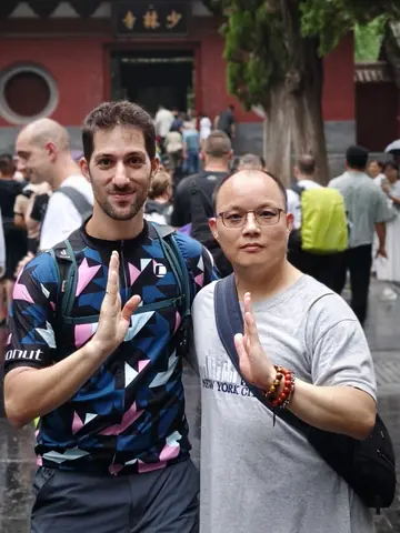 Kostis and Shaolin warrior monk Shifu Shi Heng Yi making the palm salute under the Shaolin Temple’s name board, Dengfeng, China, August 2025